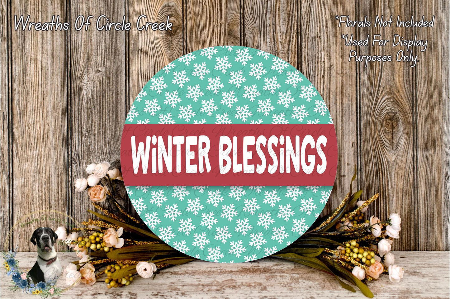 a circular sign with the text "Winter Blessings" in a red and white color scheme, surrounded by a wreath of flowers and greenery on a wooden surface.