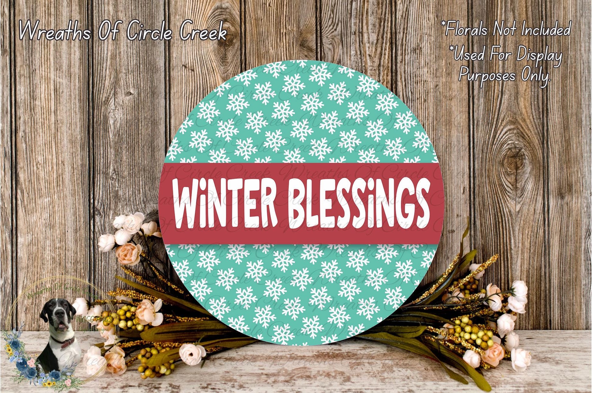 a circular sign with the text "Winter Blessings" in a red and white color scheme, surrounded by a wreath of flowers and greenery on a wooden surface.