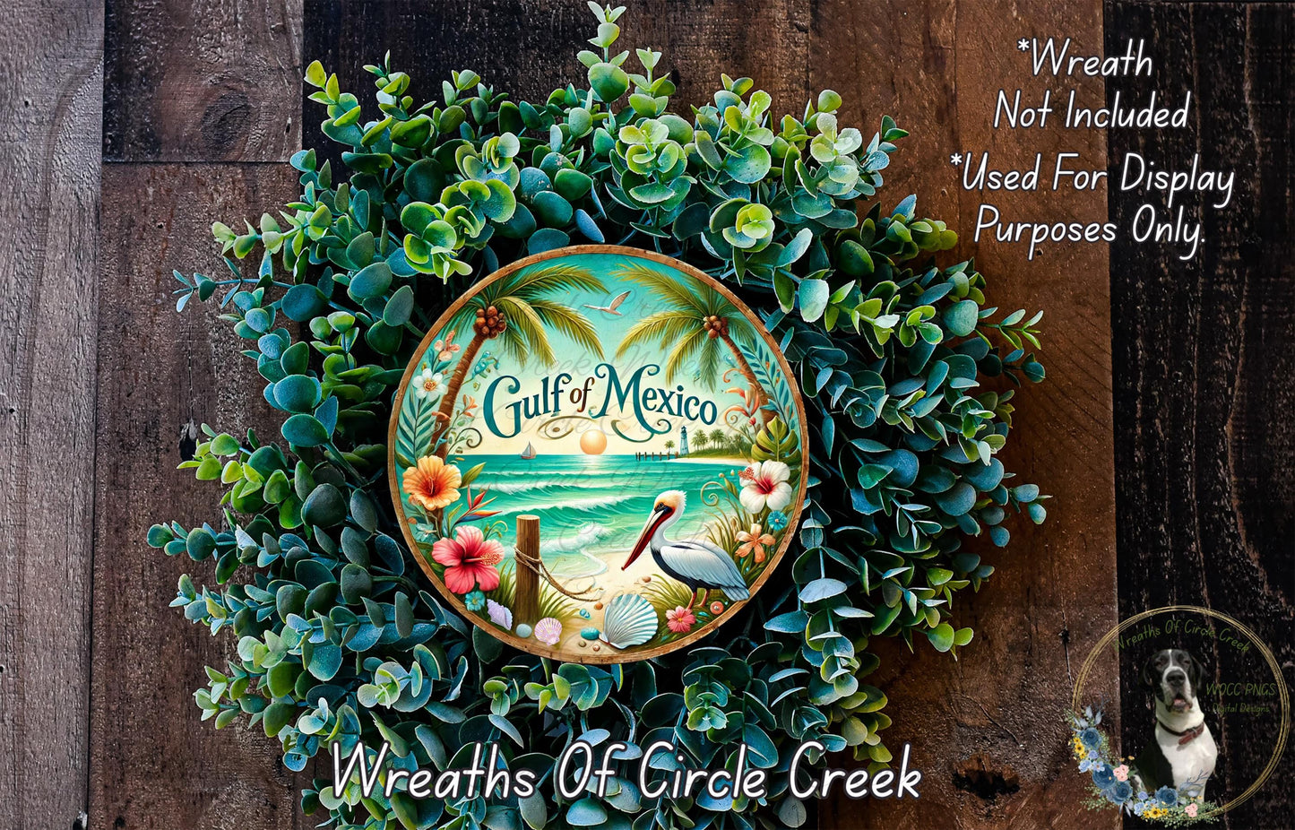 A wreath made of various green plants and flowers, with a circular plate in the center that says "Gulf of Mexico". The wreath is displayed on a wooden surface, and there is a small dog in the bottom right corner.