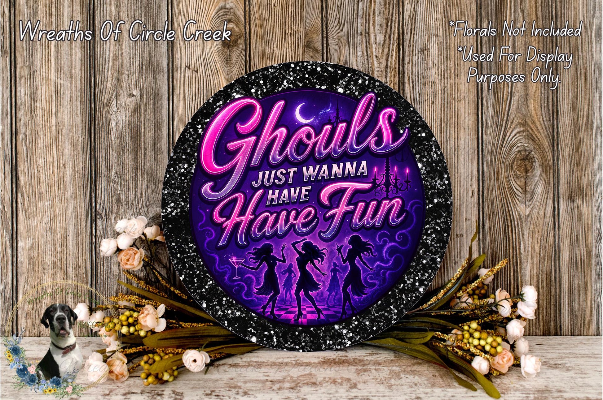 a decorative sign with the text "Ghouls Just Wanna Have Fun" in a purple and black color scheme, surrounded by a floral arrangement and a wooden background.