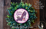 A wreath made of green leaves and a purple high heel shoe with the text "Birthday Queen" on it, placed on a wooden surface.