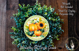 a wreath made of various autumn-themed elements, including pumpkins, gourds, and greenery. The wreath is displayed on a wooden surface, and there is a small dog in the bottom right corner of the image.