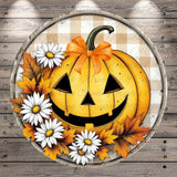 A Halloween-themed pumpkin decoration with a bow, surrounded by white daisies and autumn leaves, set against a wooden background.