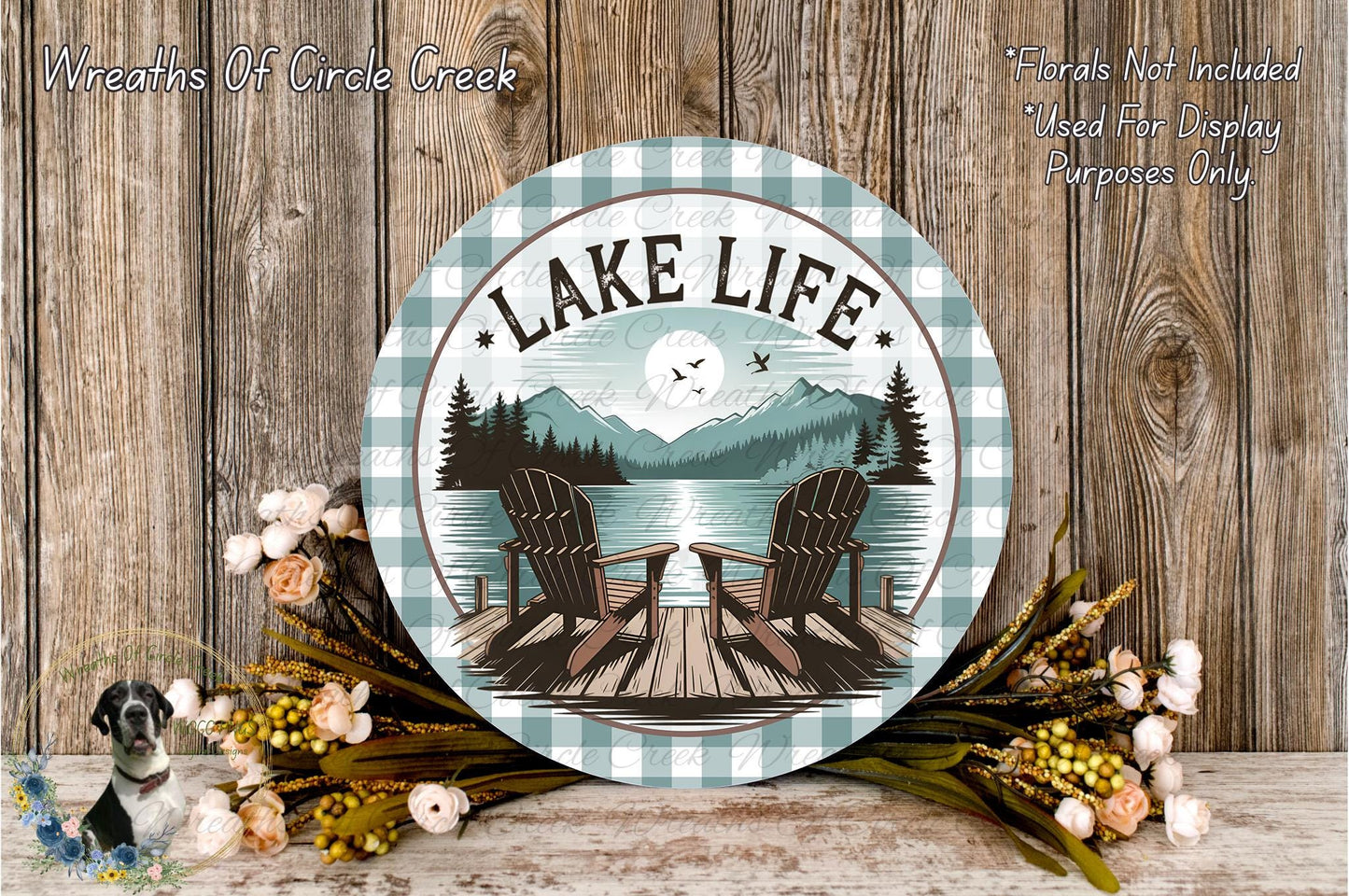 A round wooden sign with the text "LAKELIFE" and an illustration of a lake with two Adirondack chairs, surrounded by flowers and a mountain landscape.