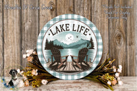 A round wooden sign with the text "LAKELIFE" and an illustration of a lake with two Adirondack chairs, surrounded by flowers and a mountain landscape.