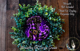 A wreath made of green leaves and purple flowers, with a purple and gold witch's boot displayed on a circular plate in the center.