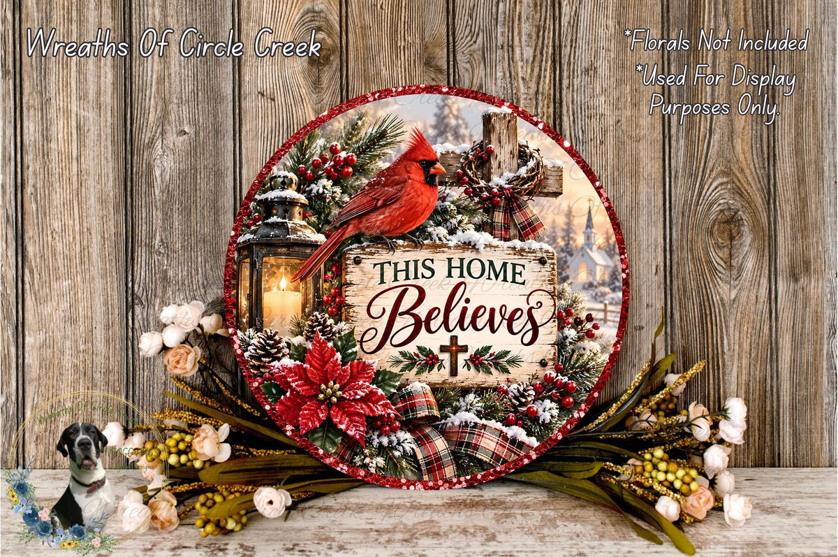 A decorative wreath with a red cardinal perched on a lantern, surrounded by pine cones, poinsettias, and a sign that reads "This Home Believes". The wreath is set against a rustic wooden background, and there are additional floral arrangements nearby.