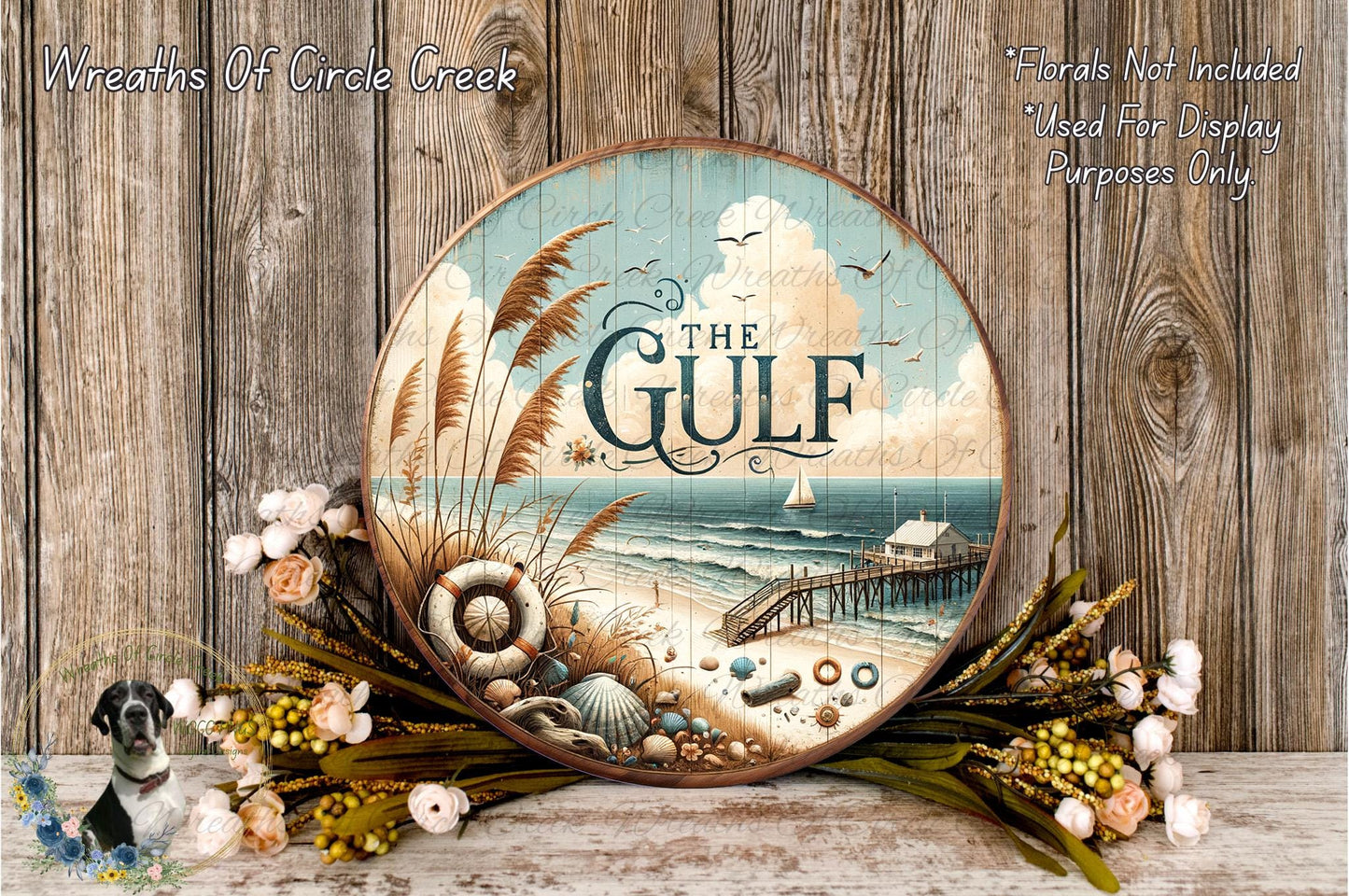 a round wooden plaque with a beach scene and a lighthouse, surrounded by flowers and placed on a wooden surface.
