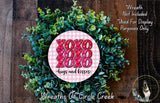 a wreath made of green leaves and a pink circular sign with the text "XOXO hugs and kisses" in the center.