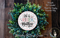 a wreath made of green leaves and flowers, with a circular sign in the center that reads &quot;He is risen Matthew 28:6&quot;.