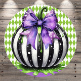 A whimsical illustration of a black and white striped pumpkin with a purple bow, set against a green and white diamond patterned background.