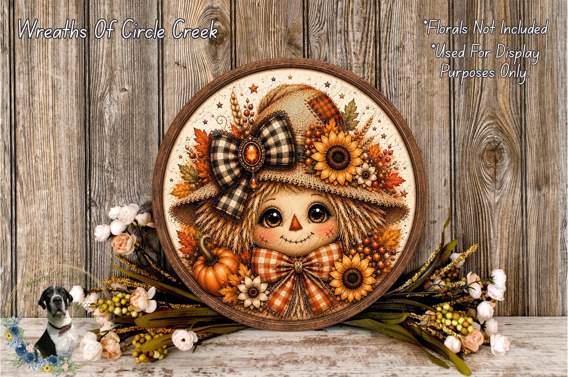 A decorative wreath featuring a scarecrow with a bow and hat, surrounded by autumn foliage and flowers, placed on a wooden surface.