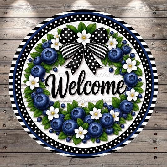 A decorative wreath with a black and white polka dot border, featuring blueberries, white flowers, and green leaves. The word "Welcome" is prominently displayed in the center of the wreath.