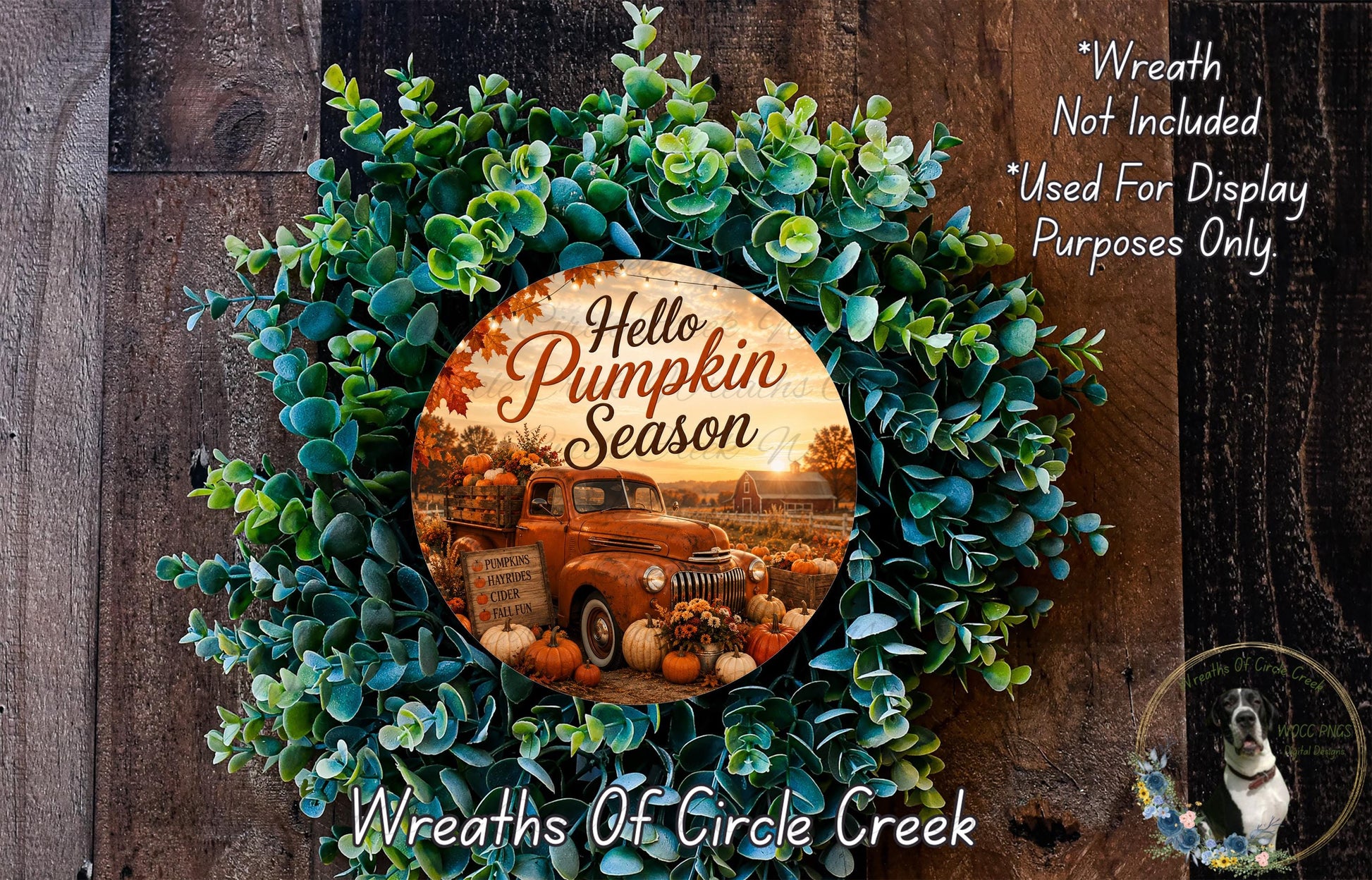 a wreath with a pumpkin and fall-themed design, surrounded by greenery. The wreath is placed on a wooden surface, and there is a small dog in the bottom right corner of the image.