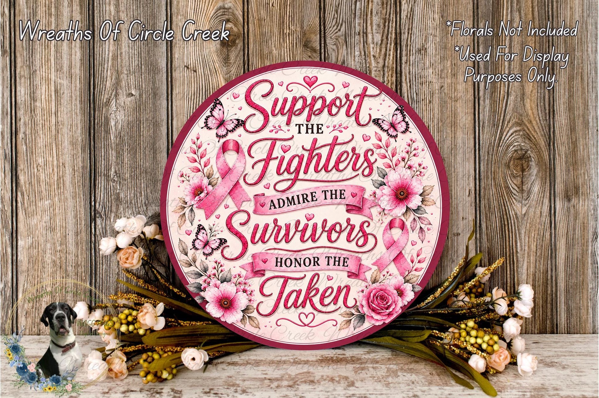 a round sign with a pink ribbon design, surrounded by flowers and placed on a wooden surface. The sign has a message that reads "Support the fighters, admire the survivors, honor the taken".