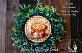 A wreath made of green leaves and featuring a pie, apples, and a candle, with the text "Happy Thanksgiving" displayed on it.