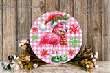 A pink flamingo wearing a Santa hat and scarf is surrounded by snowflakes and greenery, with a wooden background.