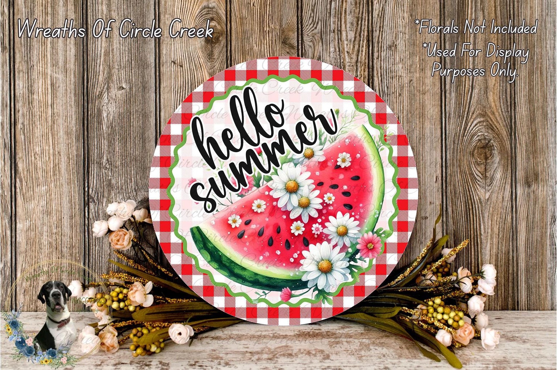 A round sign with the text "Hello Summer" and a watermelon graphic, surrounded by flowers and placed on a wooden surface.