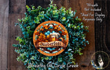 a wreath made of green leaves and a beer mug, with the word "Oktoberfest" written on it. The wreath is displayed on a wooden surface, and there is a small dog in the bottom right corner of the image.