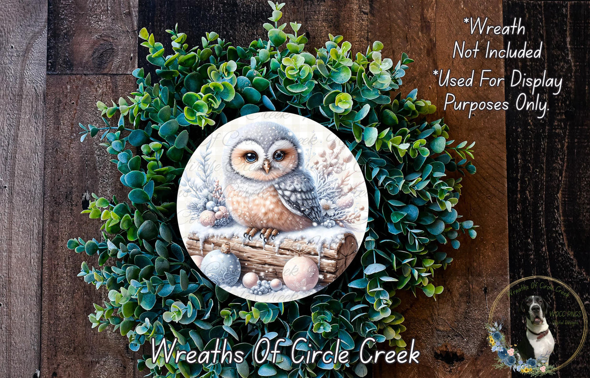 A wreath featuring a painted owl sitting on a log, surrounded by green foliage.