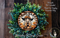 A Halloween wreath made of green succulents and featuring a cartoon illustration of a witch with a black cat. The wreath has a "Happy Halloween" message and is displayed on a wooden background.