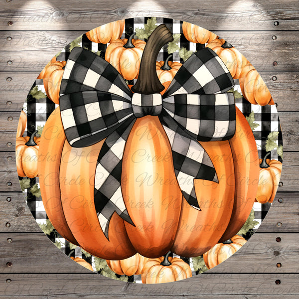 A large, orange pumpkin with a black and white checkered bow tied around it, surrounded by additional orange pumpkins and leaves against a wooden background.