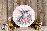 a round, decorative plate with a colorful hummingbird surrounded by pink flowers and green leaves, placed on a wooden surface.