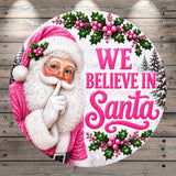 Santa Claus with a pink and white outfit, surrounded by holly leaves, berries, and the text "We believe in Santa"