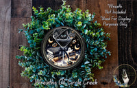 A wreath made of green leaves and a black cat wearing a witch's hat, with a clock face in the center.