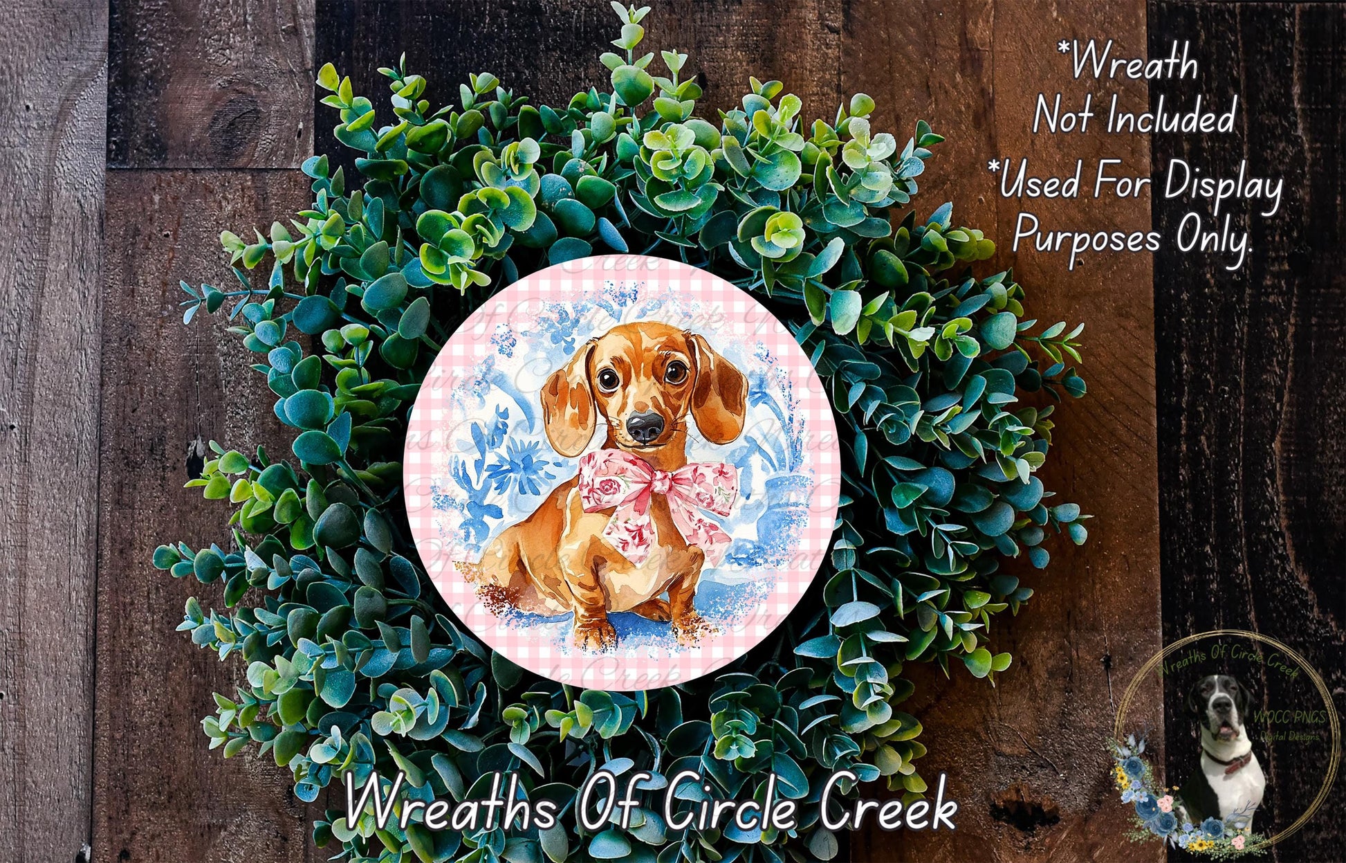 A wreath made of green plants and a pink and blue floral design, featuring a dachshund dog wearing a pink bow.