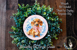 A wreath made of green plants and a pink and blue floral design, featuring a dachshund dog wearing a pink bow.