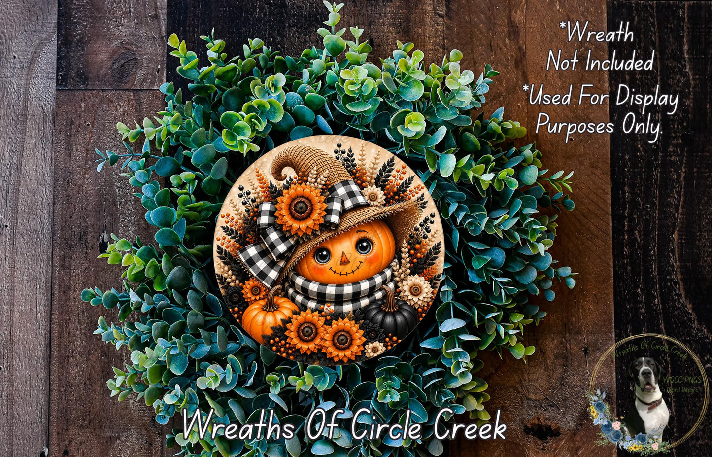 a wreath with a pumpkin and a scarecrow design, surrounded by green foliage. The wreath is displayed on a wooden surface, and there is a small dog in the bottom right corner of the image.