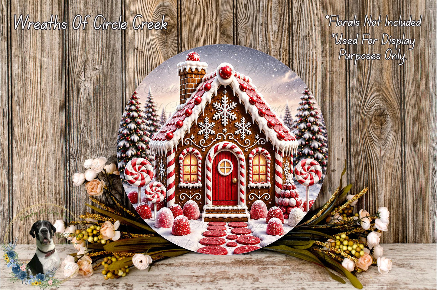 A round wooden plaque depicting a gingerbread house surrounded by flowers and greenery, with a snowy winter landscape in the background.