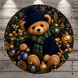 A teddy bear wearing a blue hat and scarf sits amidst a festive arrangement of Christmas ornaments, presents, and pine cones.