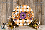 a Halloween-themed decoration with a large circular sign that says "Boo" in orange and purple colors, surrounded by a spider web, bats, and pumpkins. The decoration is placed on a wooden surface, with a wreath of flowers and a spooky spider decoration nearby.