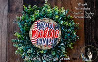 a wreath made of green leaves and a circular sign with the text "Proud Marine Family" in red and blue colors. The wreath is displayed on a wooden surface, and there is a small dog in the bottom right corner of the image.