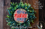 a wreath made of green leaves and a circular sign with the text "Proud Marine Family" in red and blue colors. The wreath is displayed on a wooden surface, and there is a small dog in the bottom right corner of the image.