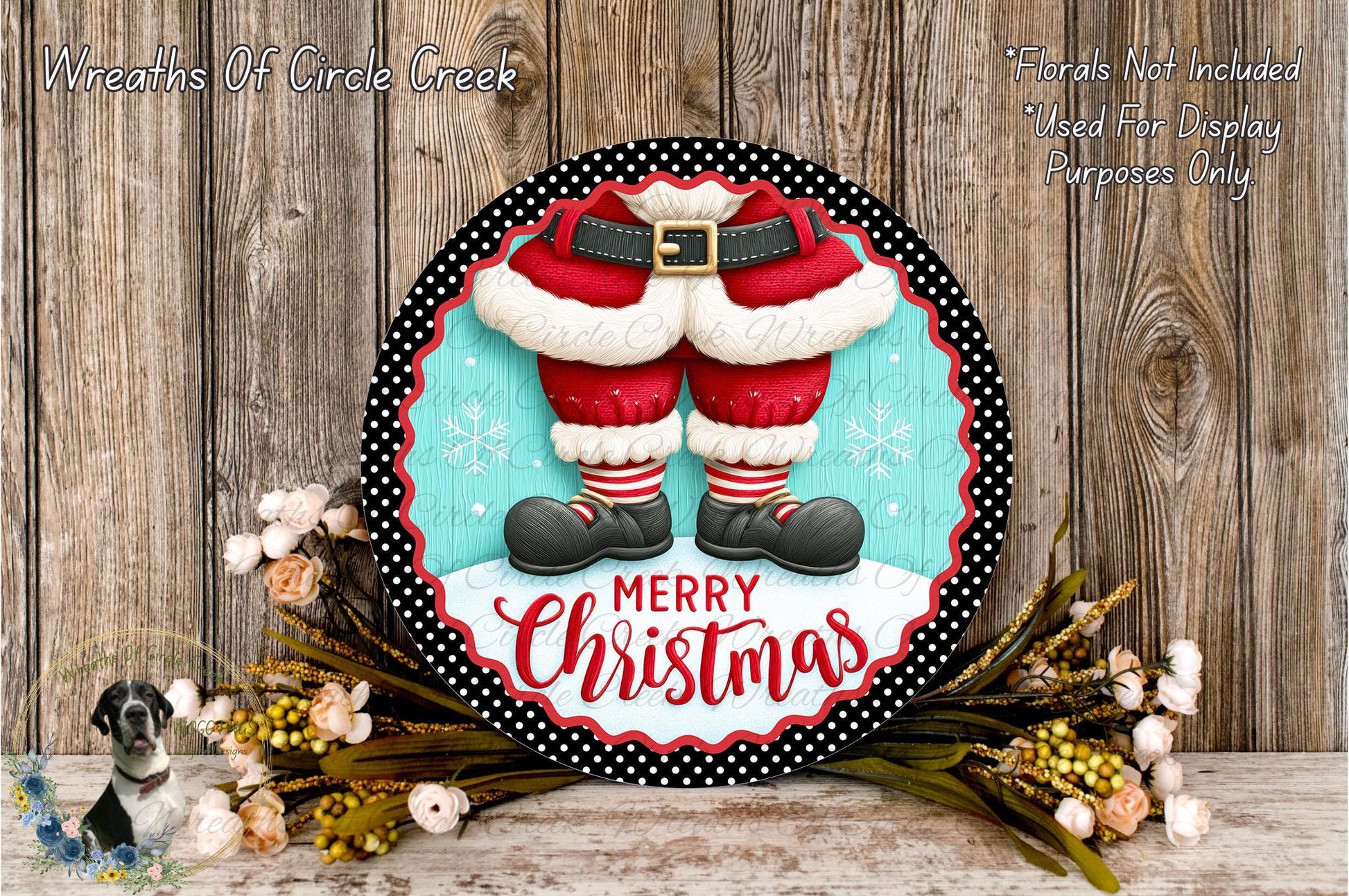 A festive Christmas wreath with a Santa Claus figure wearing red and white pants, surrounded by flowers and greenery. The wreath has the text "Merry Christmas" written on it.