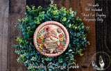 a wreath with a gnome holding a sign that says "Welcome Friends" surrounded by green foliage.