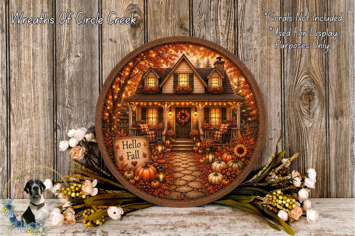 A round wooden frame displaying a painting of a house surrounded by fall decorations, including pumpkins, flowers, and a wreath.