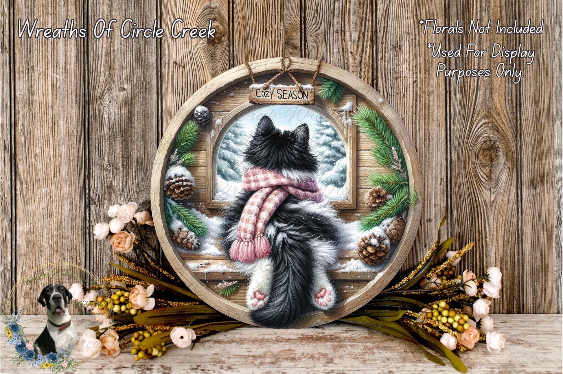 A black and white cat is sitting on a wooden bench, looking out through a window, with a wreath of pine cones and flowers surrounding it.
