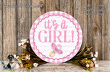 a round sign with the text "It's a girl!" surrounded by a floral arrangement and a wooden background.