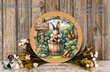 A round wooden plaque with a bunny sitting in a wooden barrel, surrounded by flowers and carrots, against a wooden background.