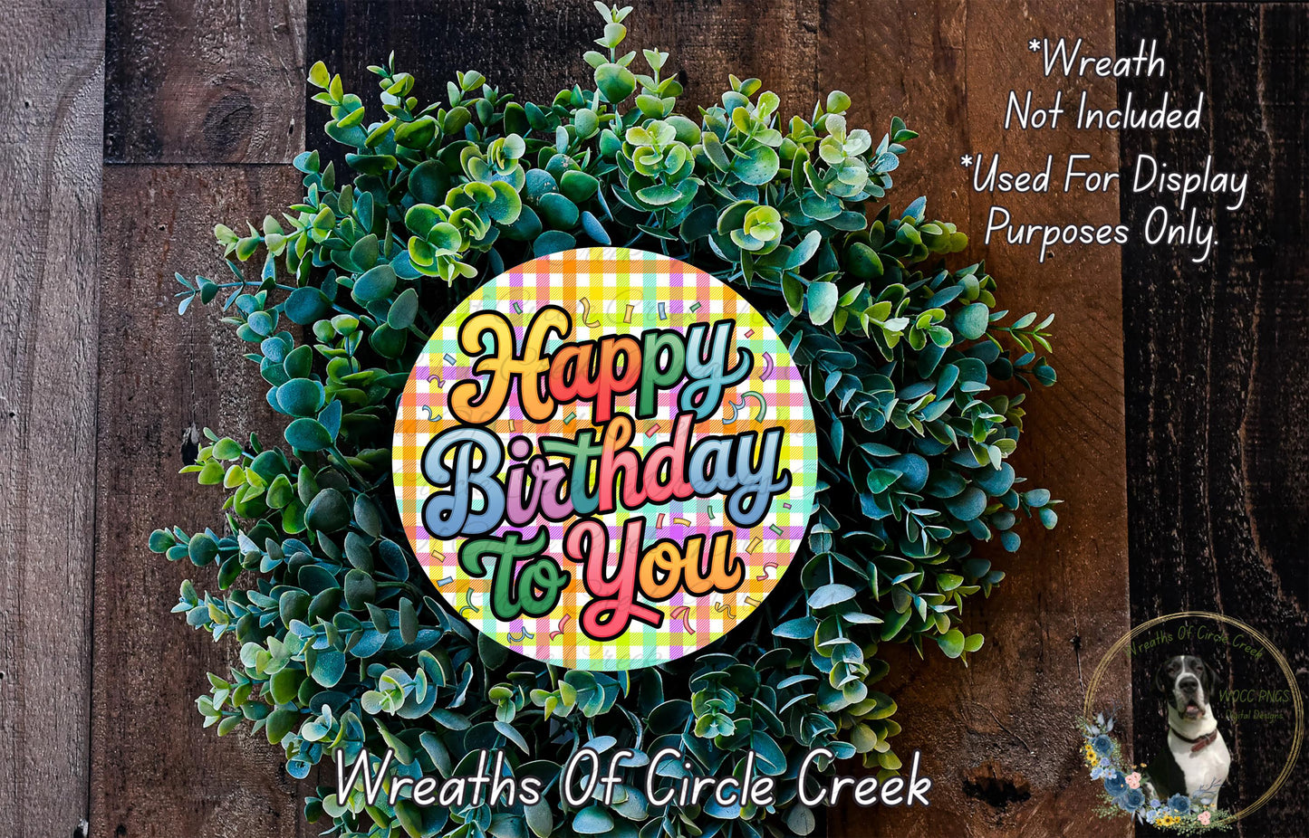 a wreath made of green leaves and a colorful circular sign that says "Happy Birthday to You". The sign is surrounded by the wreath, which is placed on a wooden surface.