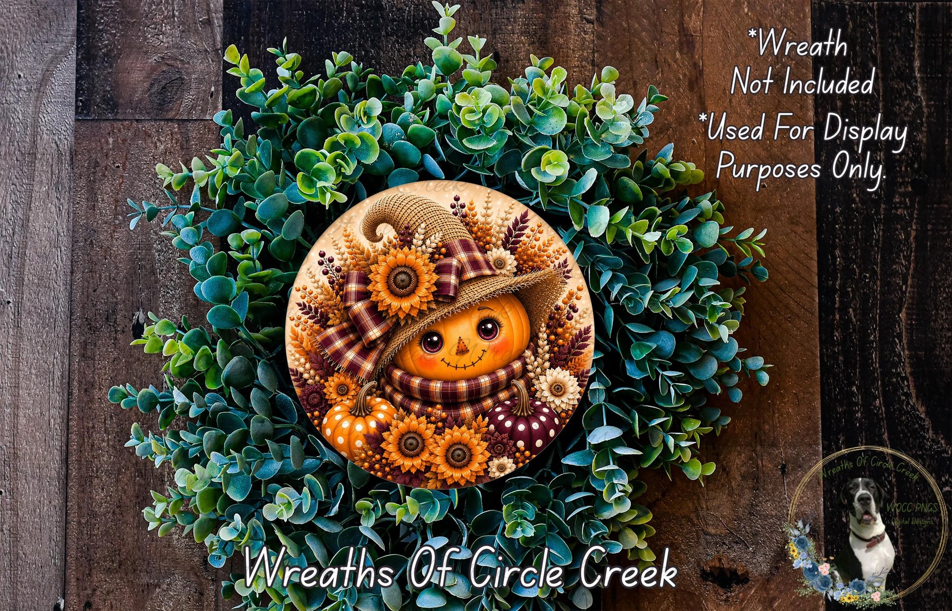 a wreath with a pumpkin face and a plaid hat, surrounded by green foliage. The wreath is displayed on a wooden surface, and there is a small dog in the bottom right corner of the image.