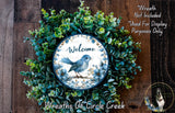 a wreath with a blue bird on a branch, surrounded by green foliage. The wreath is displayed on a wooden surface, and there is a text overlay that reads "Welcome Wreath Not Included * Used For Display Purposes Only" and "Wreaths Of Circle Creek".