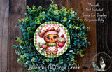 A wreath featuring a gingerbread man holding a cupcake, surrounded by a lush green plant.
