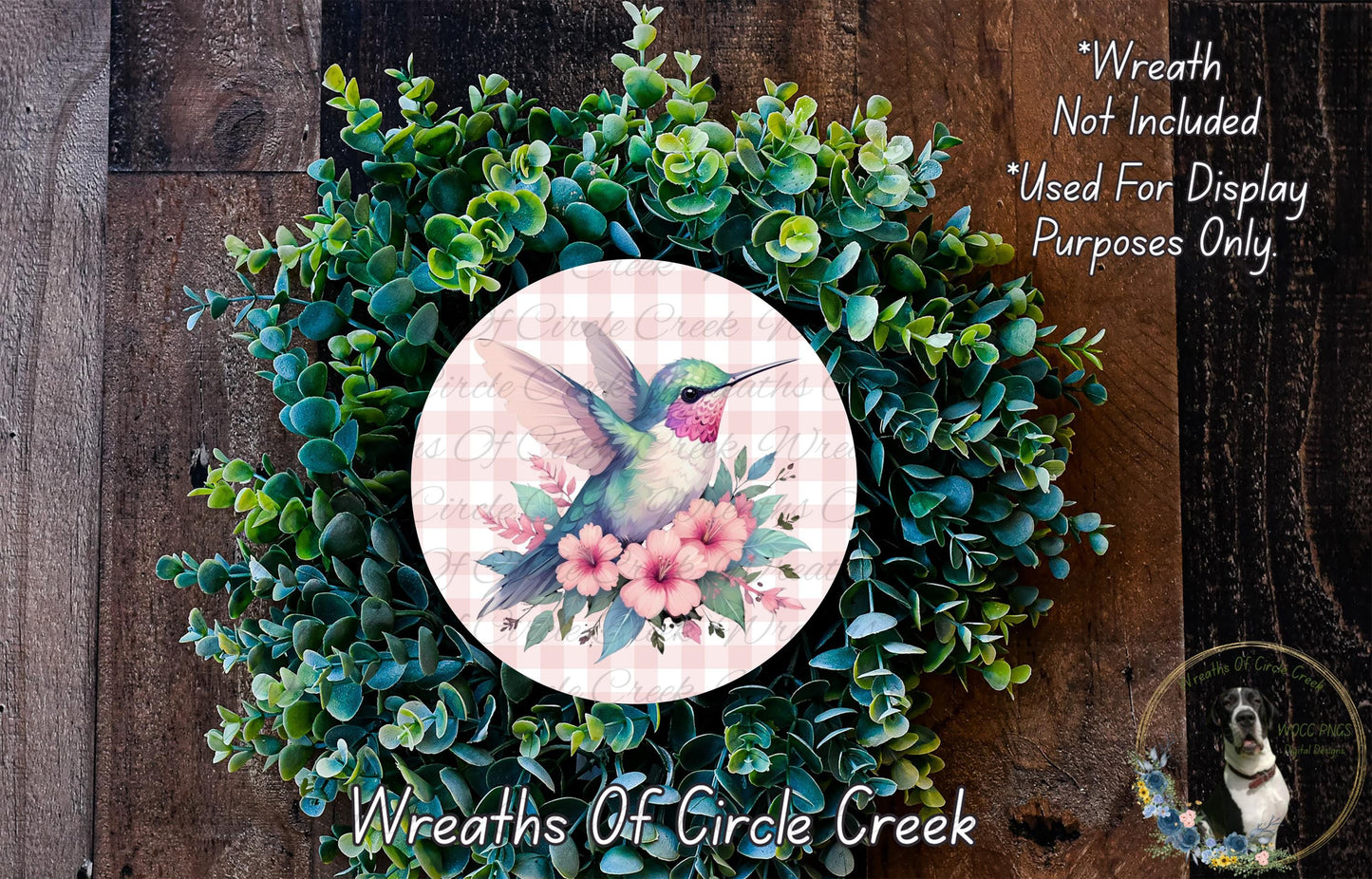 a wreath with a hummingbird and flowers, surrounded by greenery. The wreath is placed on a wooden surface.