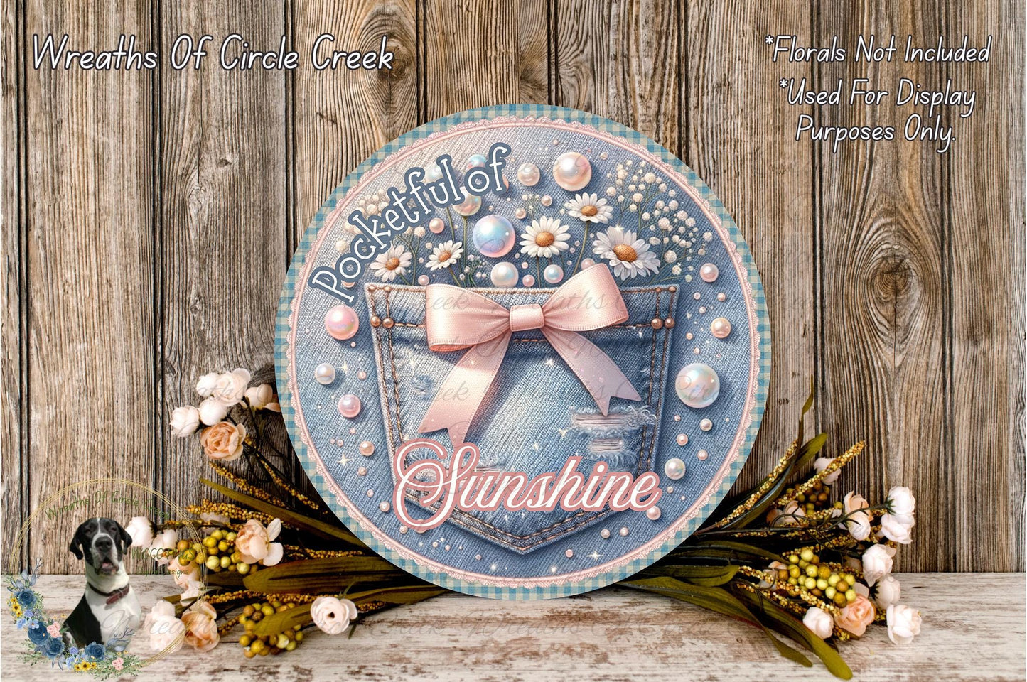 a decorative round sign with a floral design, surrounded by flowers and placed on a wooden surface.