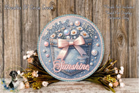 a decorative round sign with a floral design, surrounded by flowers and placed on a wooden surface.